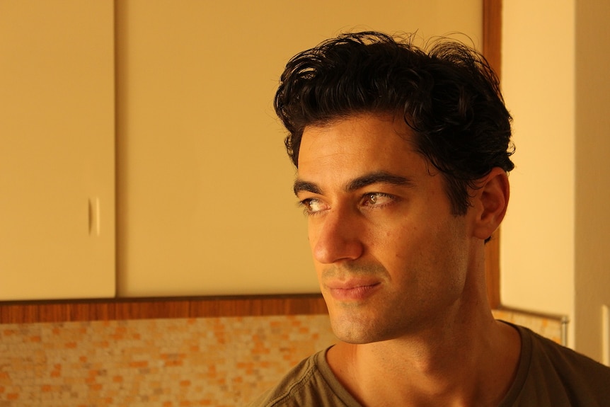 A man with dark hair and brown eyes looks to his right in a kitchen