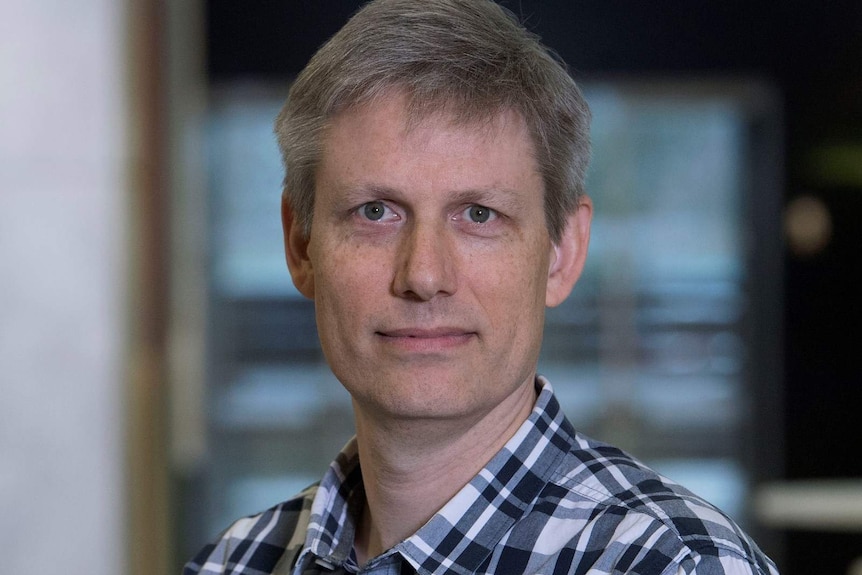 a man in a collared chequered shirt looking into the camera