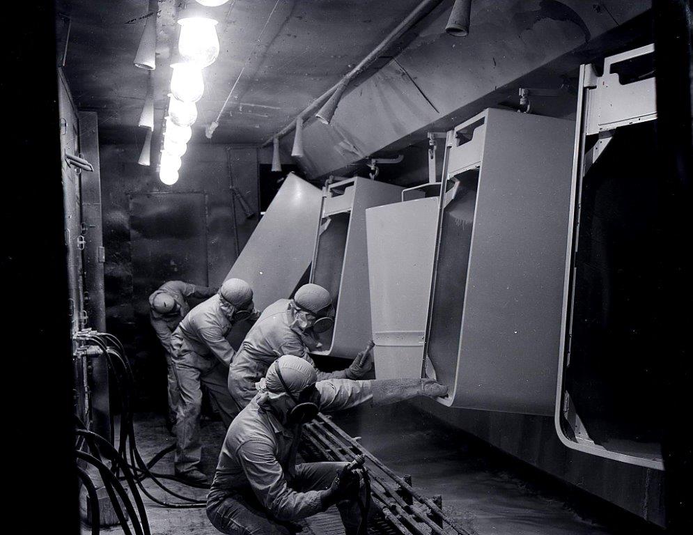 A black and white photograph of people in protective suits and masks working on fridges