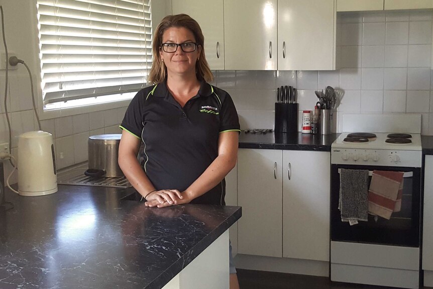 A mid-shot of Rockhampton resident Leticia Jukes standing in the kitchen of her home smiling and posing for a photo.
