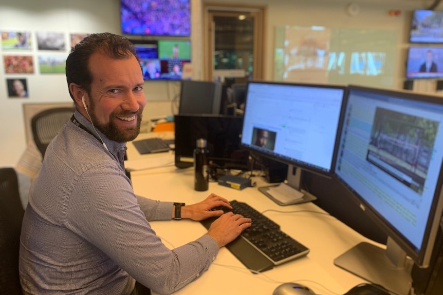 Smale sitting at computer screens with headphones on looking at camera and smiling.