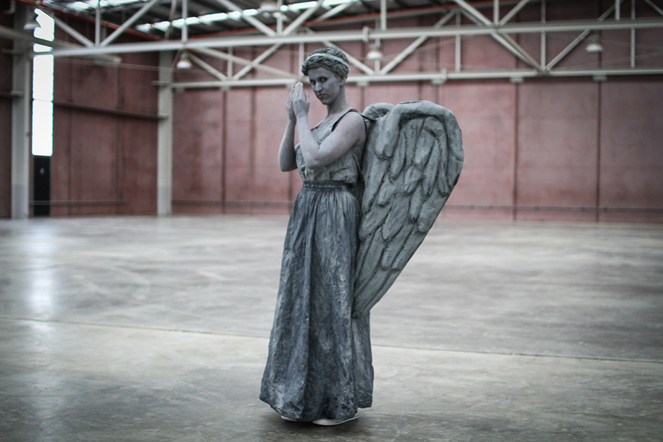 A woman painted grey, with a grey dress and wings.