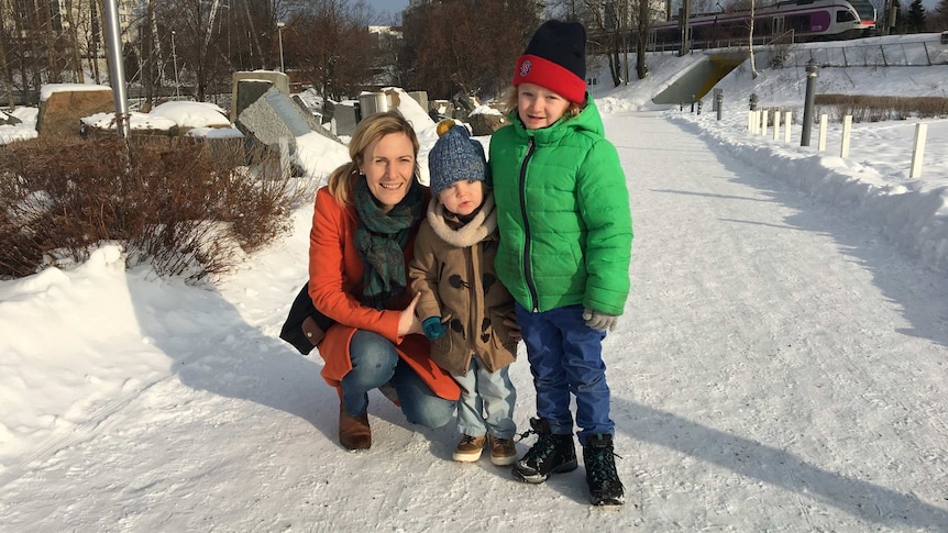 A mother and two young boys kneel in the snow with a train passing behind them.