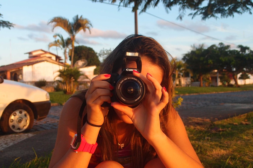 A woman holding a camera up to her face, taking a picture.