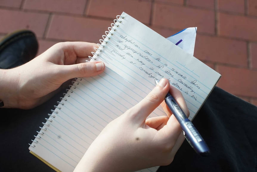 Findlay's hand is seen writing on a page with a black pen. Four lines of text have been written, some words spelled wrong