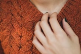 A woman in knit jumper, with her hand to her neck.