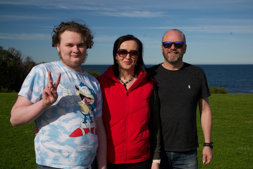 Two parents with a teenager holding the peace sign standing outside.