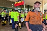 Bearded man in high-vis gear stand in front of protesters.