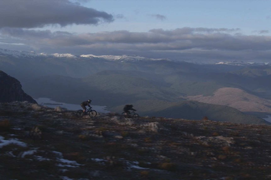 Two mountain bikers on summit of Mt Owen, views to snowy peaks