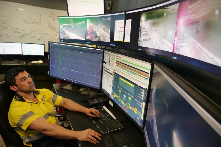 A man in a high-vis shirt sitting down in front of a wall of computers, looking at them