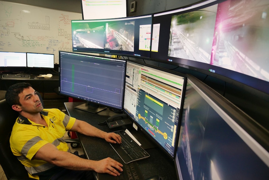 A man in a highly reflective shirt sits in front of a computer wall and looks at them