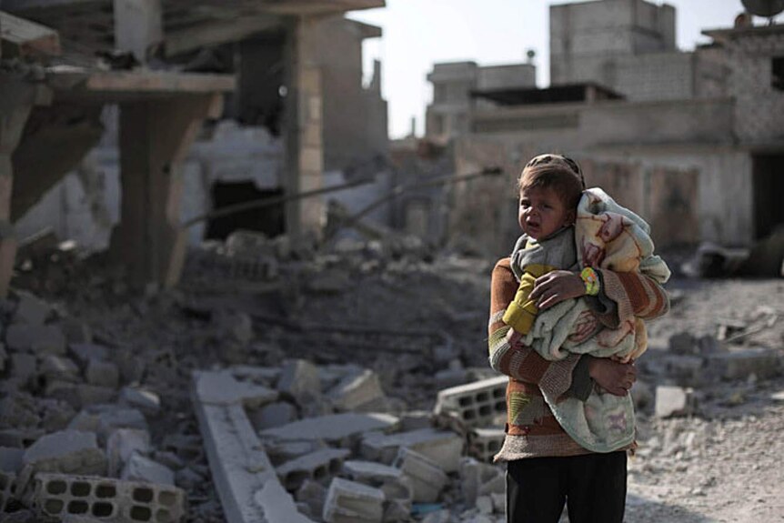 A toddler cries amidst the debris of buildings destroyed by airstrikes.