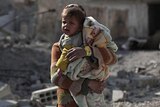 A toddler cries amidst the debris of buildings destroyed by airstrikes.