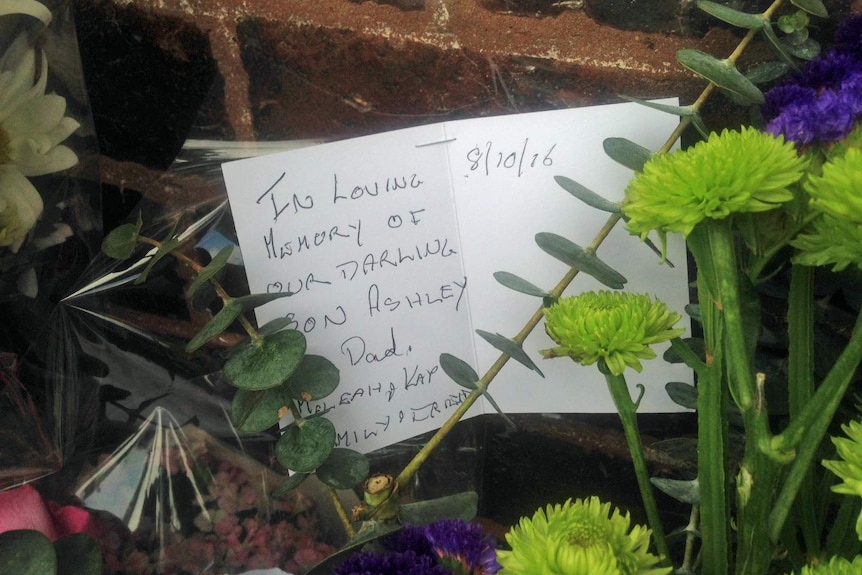 A card sits in flowers laid at the gates of Eagle Farm in memory of Ashley Morris.