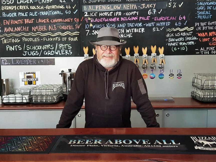 A man with a beard stands behind a bar.