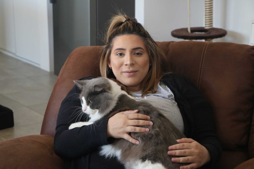 A pregnant sits on a couch petting her cat