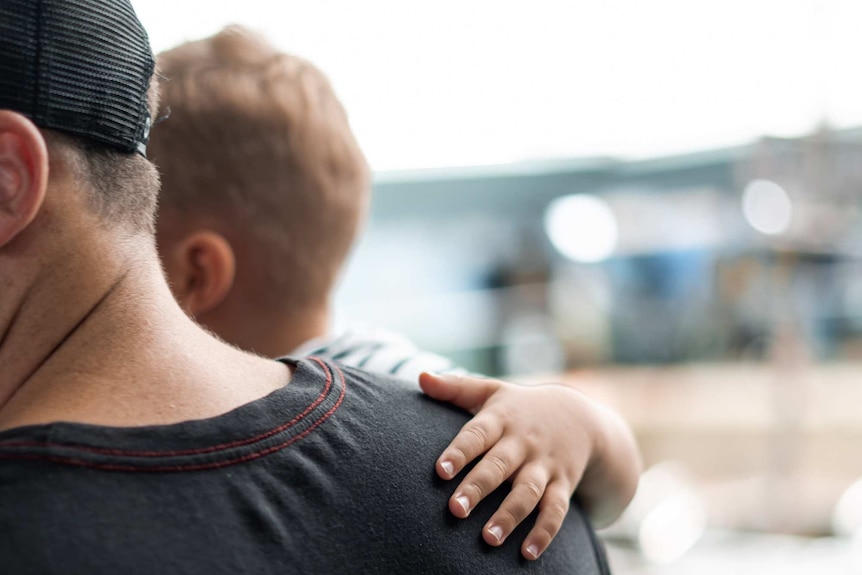 A boy puts his hand on a man's back as he holds him.