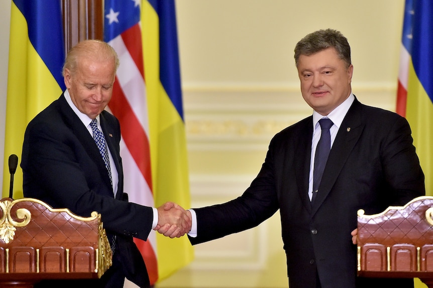 Joe Biden and Petro Poroshenko shake hands while standing at podiums with US and Ukraine flags behind them.
