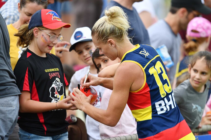 An AFLW player signs a footballer for a young fan after the game.