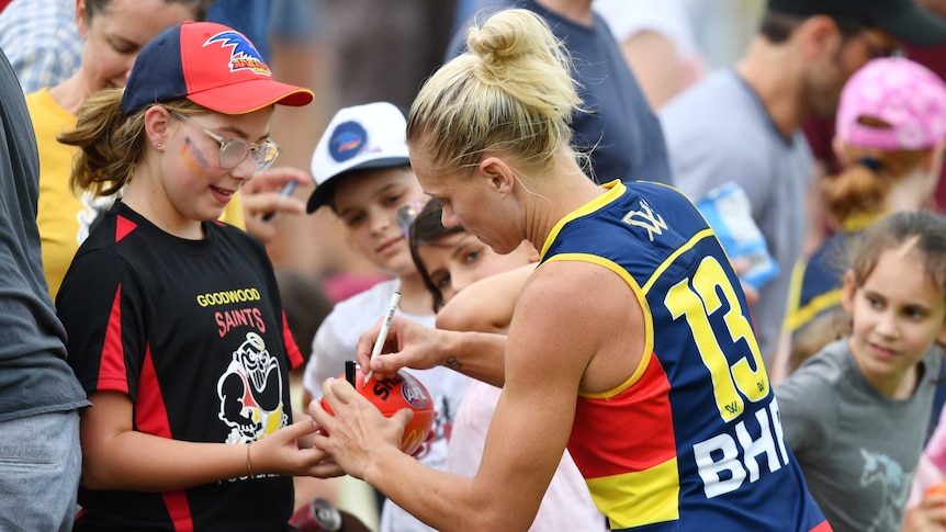 An AFLW player signs a footballer for a young fan after the game.