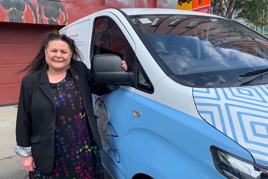 A woman wearing a black blazer standing next to a brightly-coloured van.