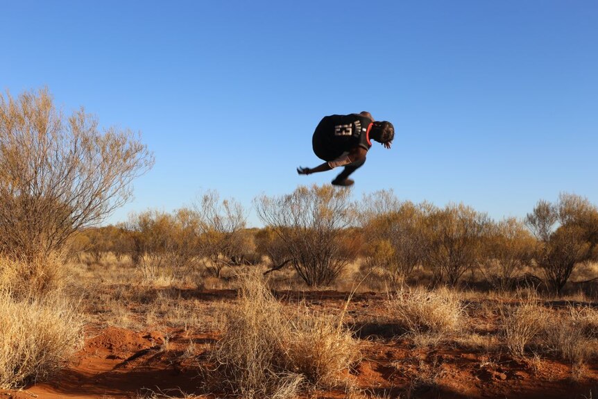 A player from the Mimili Blues does a backflip on the side of the road.