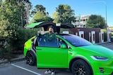 A man wearing a cap backwards stands by a bright green car, with its doors open.