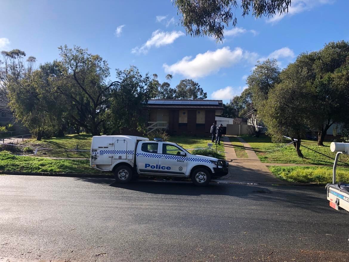 A police car parked on a road outside a house with boarded up windows.