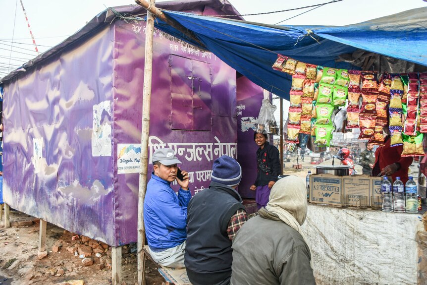 A woman stands outside a purple tent while a man talks on a mobile phone.