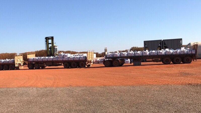 Road train truck on red dirt with bags on the back.