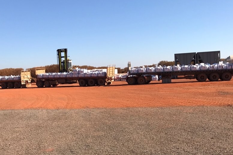 Road train truck on red dirt with bags on the back.