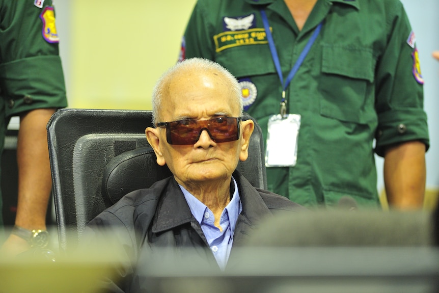 A picture of Nuon Chea with pursed lips and large dark glasses.