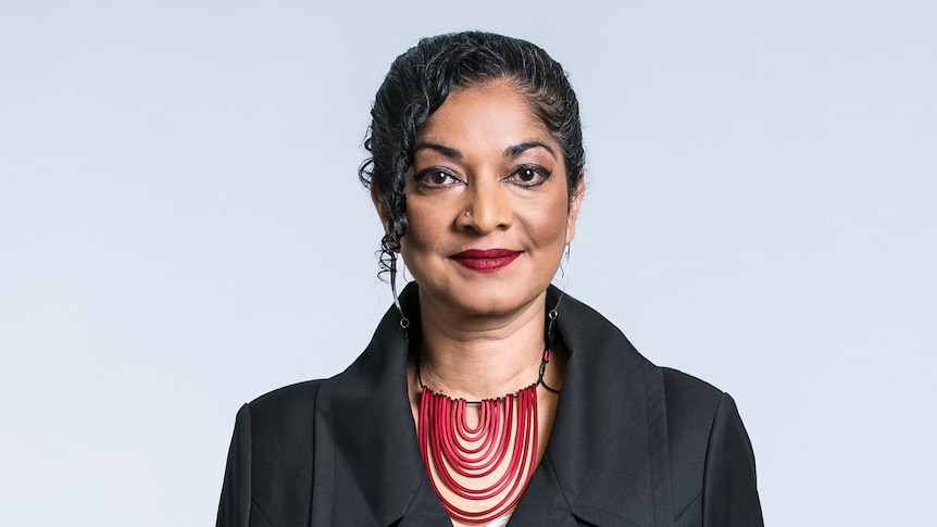 A profile image of a woman with dark hair, wearing a black suit and red necklace.