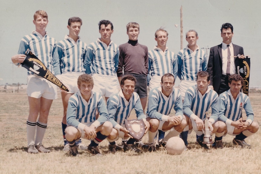 A man in a suit stands beside a soccer team dressed in blue and white jerseys.