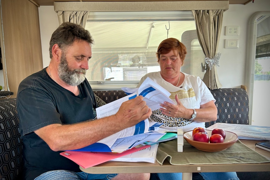 A man and a woman sit at a table in a caravan and look through insurance paperwork.