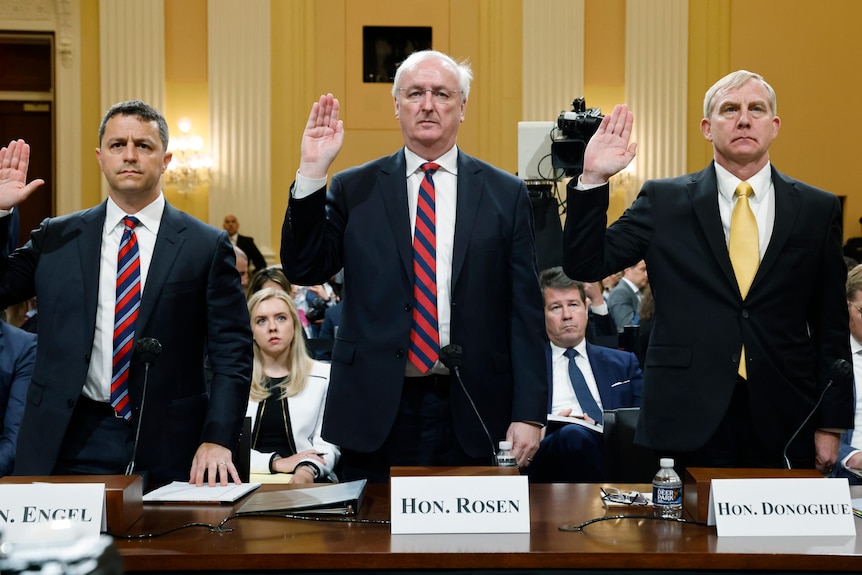Three men in suits standing behind a table with their right hands raised to take an oath 