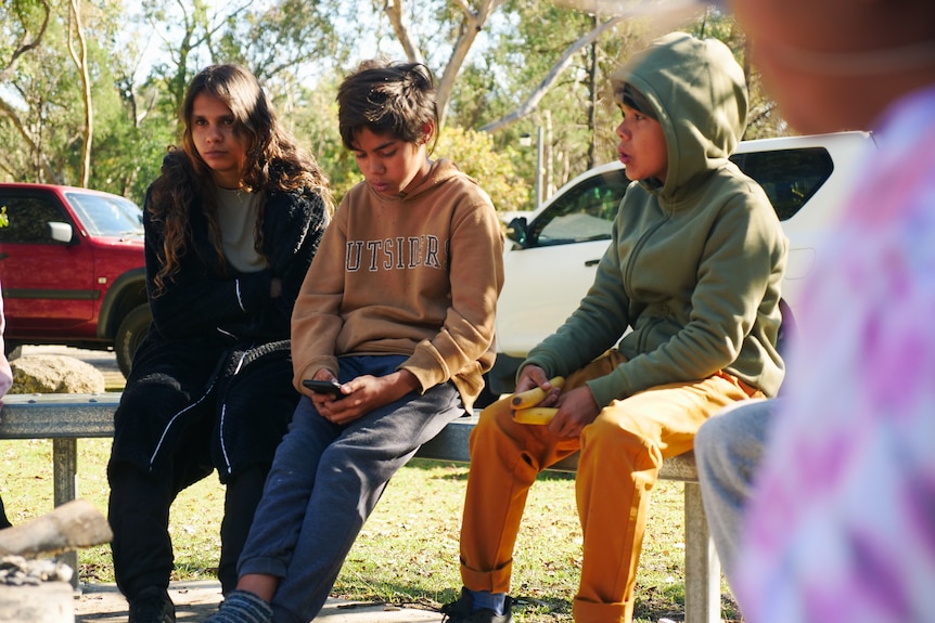Three young Indigenous kids sit on a bench in Gameroi country.