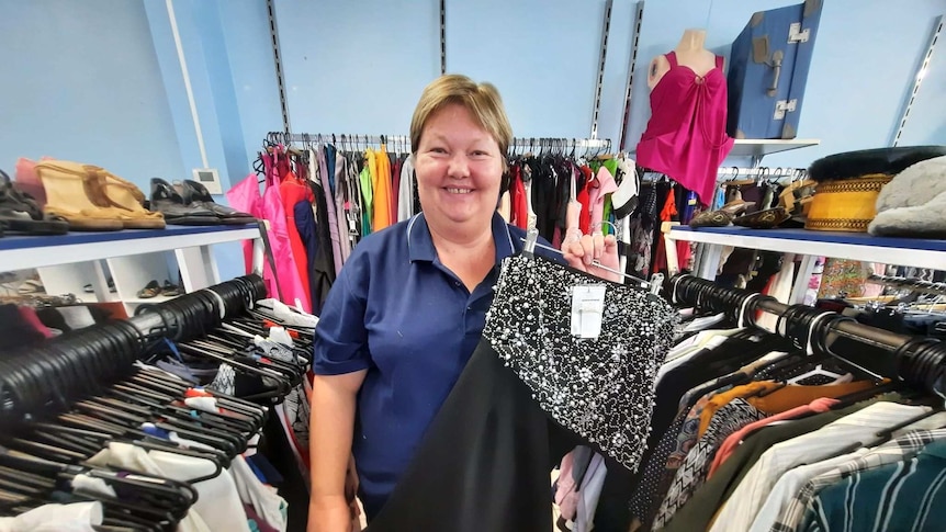 A lady with short hair holds a dress standing in a clothing store.