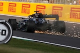 Sparks fly from a Formula One car as it speeds down a straight with a punctured tyre.