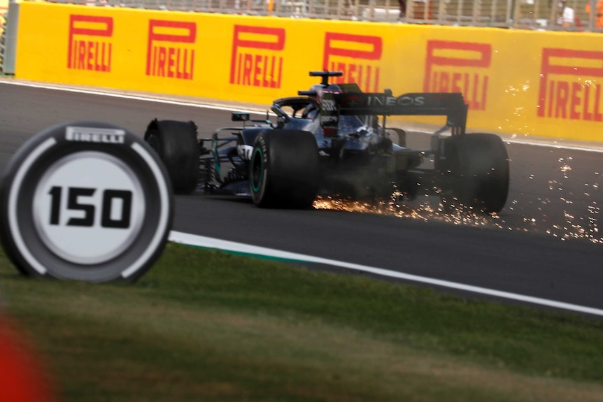 Sparks fly from a Formula One car as it speeds down a straight with a punctured tyre.
