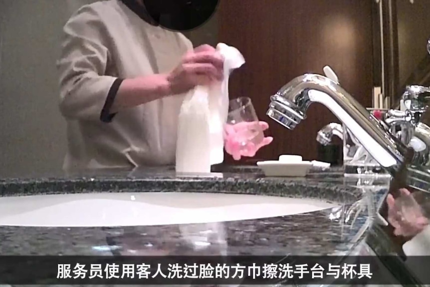 A cleaner at a hotel in China uses a soiled face towel to wash a glass. Still taken from video.