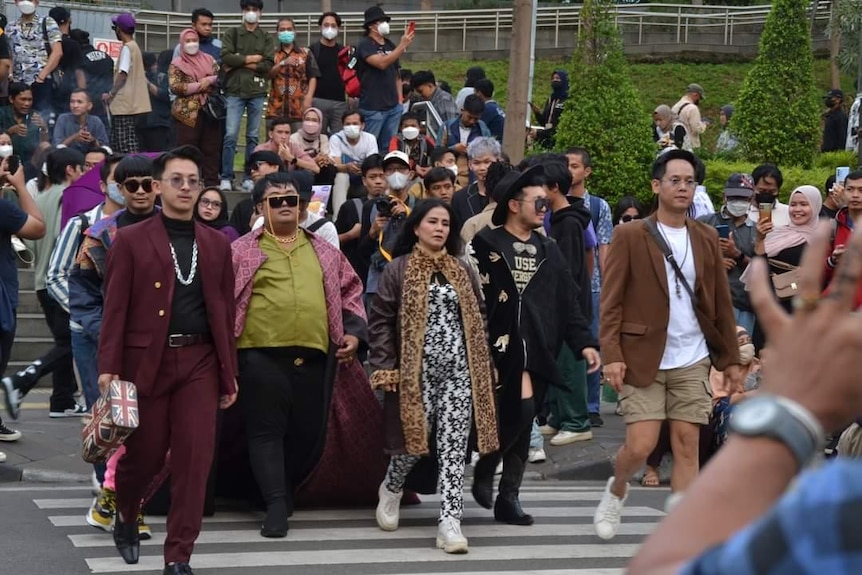 A bunch of people, men and women, wearing different style of outfits, walking in zebra crossing.