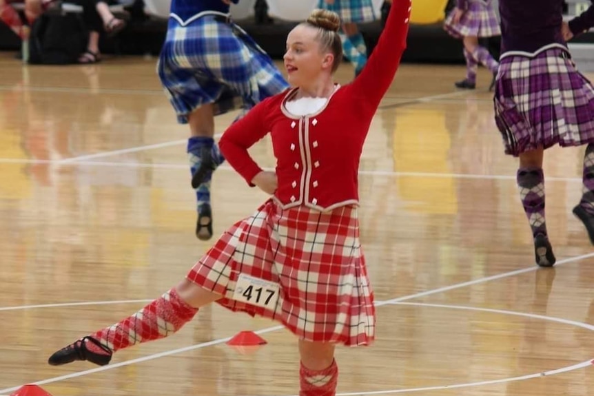 Tully Stone dressed in red top and red and white tartan while competing in a highland dancing competition.