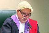 A man with glasses in a judge's wig 