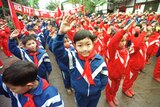 Sekelompok anak kecil yang mengenakan baju olahraga biru dan merah dengan dasi merah memberi salam ke arah kamera.