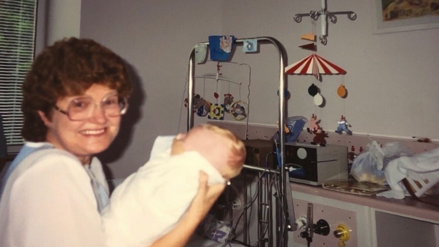 Lady with glasses holding a baby in an ICU ward.