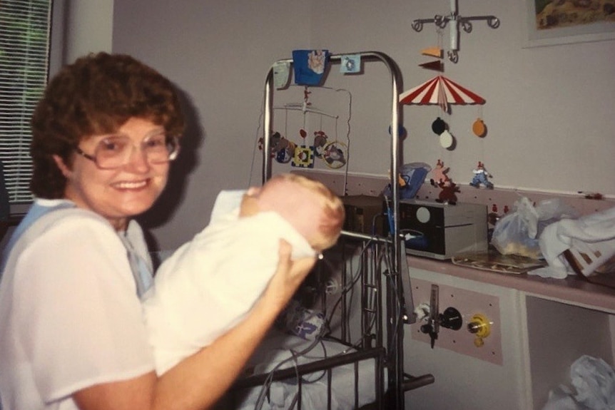Lady with glasses holding a baby in an ICU ward.