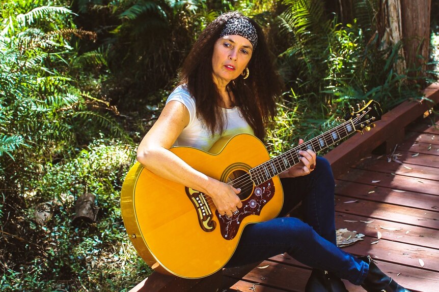Sophia Fletcher playing acoustic guitar in a garden.