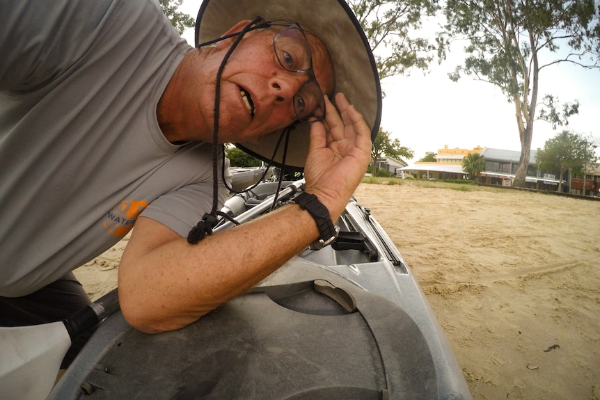 A man in glasses and a wide-brimmed hat checks the angle of his kayak-mounted camera.