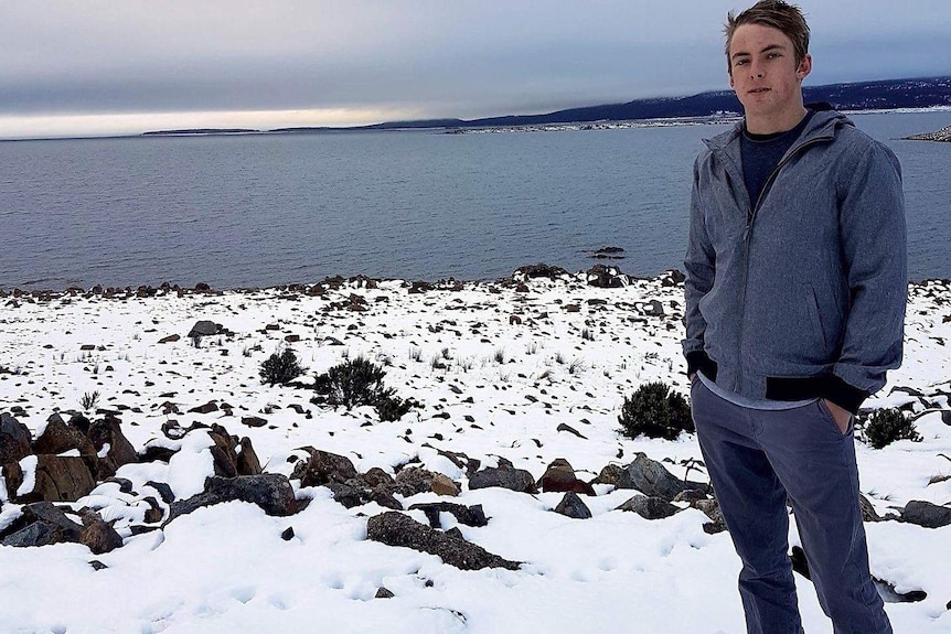 WA teenager Lloyd Dunham stands with his hands in his pockets on a snowy patch of land in front of a stretch of water.